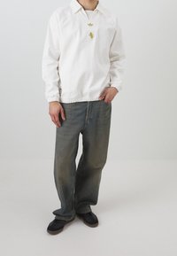 Bílý pulovr s dlouhým rukávem a límečkem, s elastickým lemem, ve spojení s volně střiženými, vybledlými modrými džíny. Doplněno dvěma vrstevnatými náhrdelníky.