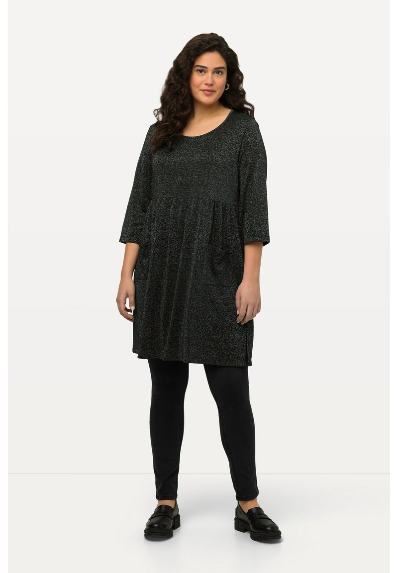 Tunique gris foncé à manches courtes, décolleté arrondi et taille froncée. Portée sur des leggings noirs et des chaussures noires à semelles épaisses. Texture lisse.