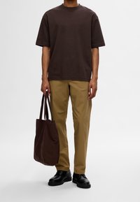 Camiseta corta de manga corta marrón combinada con pantalones rectos de color marrón claro. Un bolso de mano marrón oscuro y zapatos negros completan el conjunto.