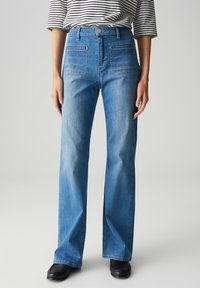 Hoge taille blauwe denim jeans met een rechte pijp, voorzien van voor- en achterzakken, en een vervaagde afwerking. Gepaard met zwarte schoenen.