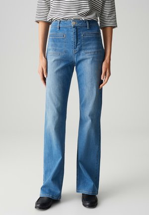 Hoge taille blauwe denim jeans met een rechte pijp, voorzien van voor- en achterzakken, en een vervaagde afwerking. Gepaard met zwarte schoenen.