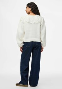 Vit tröja med en strukturerad spetskrage, ballongärmar och ribbad fåll. Kombinerad med mörkblå vida jeans och bruna skor.