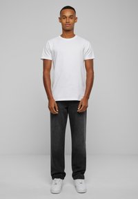 White cotton t-shirt with short sleeves, paired with dark gray denim trousers, complementing white sneakers, standing against a plain backdrop.