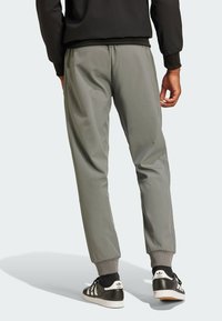 Gray tapered track pants with elastic cuffs. Smooth texture, side stripes, and a matte finish. Worn with black and white athletic shoes.