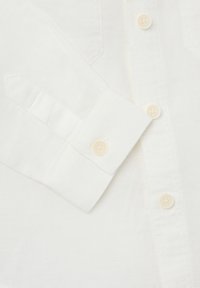 Witte linnen shirt met een knoopsluiting aan de voorkant, met een puntige kraag, knoopmanchetten en zichtbare stiksels op de stof.