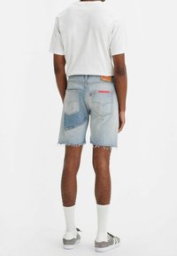 jeanshorts med en ljusblå tvätt, fransad nederkant och en unik lapptäckesdesign. Matchas med en enkel vit t-shirt och grå skor.