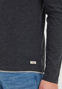 Langærmet skjorte lavet af mørkegrå stof med en blød tekstur. Har en lys grå kant og et lille mærke forneden med "BLEND DENIM."