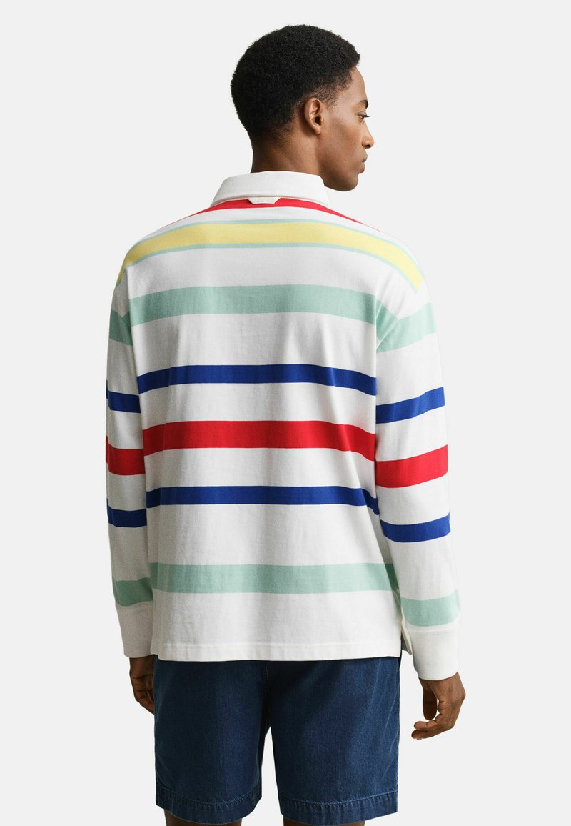 Uomo di spalle che indossa una polo a maniche lunghe con strisce orizzontali rosse, blu, verdi e gialle e pantaloncini blu scuro.