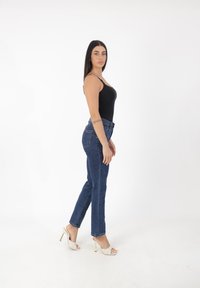 Czarny dopasowany tank top, niebieskie dżinsowe spodnie z wysokim stanem oraz białe sandały na obcasie. Stylizacja ma smukły, casualowy fason z minimalną ilością detali.