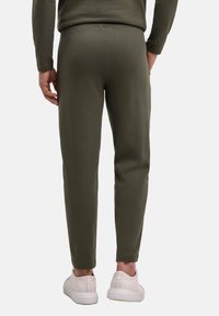 Olivgrüne, gerippte Jogginghosen mit schmal zulaufendem Schnitt, ausgestattet mit einem elastischen Bund und einem Mann, der weiße Turnschuhe trägt.