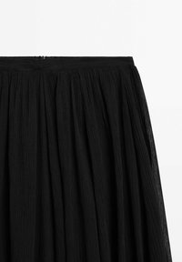 Jupe plissée noire en tissu texturé, taille ajustée et légère fermeture éclair au centre supérieur.
