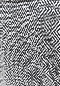 Tessuto intrecciato in bianco e nero con un motivo geometrico a diamante. La texture è liscia con un aspetto strutturato.