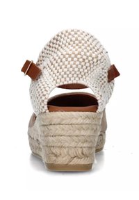 Sandalo con zeppa, superiore intrecciato di un leggero beige, dettagli in pelle marrone e tacco avvolto in juta. Apertura sul retro e dettaglio della fascia alla caviglia.