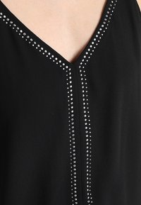 Top senza maniche nero con scollatura a V, adornato da righe verticali di strass sul davanti per un tocco di eleganza e texture.