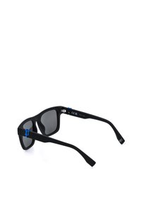 Lunettes de soleil rectangulaires noires avec verres foncés et accents bleus aux charnières, présentées de profil sur fond blanc.