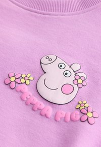Tela morada con una cara de cerdo de dibujos animados, mejillas rosas, rodeada de flores rosas y amarillas, con el texto "PEPPA PIG" debajo de la imagen.