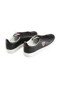 Zwarte leren sneakers met witte rubberen zolen, voorzien van zwarte veters, een rood en blauw accent op de tong en een logopatch aan de zijkant.