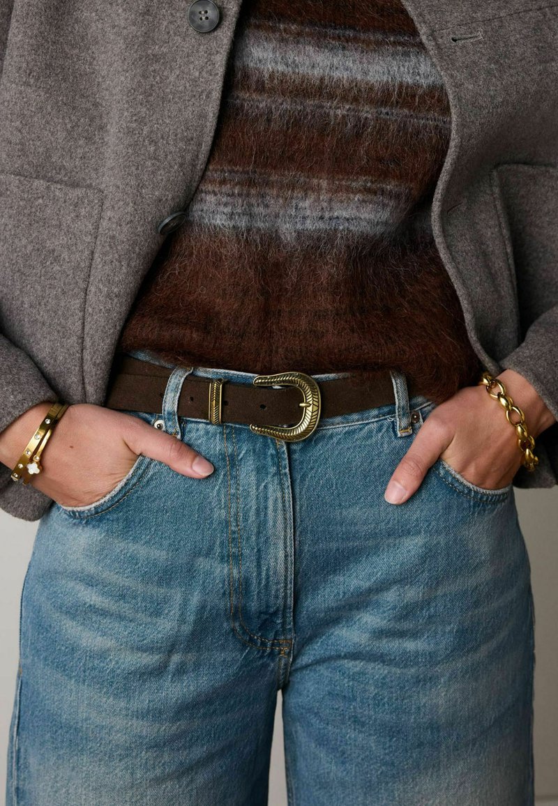 Bruine leren riem met gouden metalen gesp, grijze gestructureerde blazer, bruin gestreepte trui en lichtblauwe denim jeans. Minimale hardwaredetails.