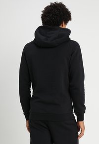 Sudadera con capucha negra, hecha de un tejido suave, que incluye un bolsillo tipo canguro y puños acanalados. Diseño sencillo con un corte clásico.
