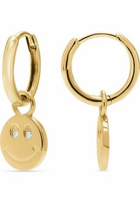 Orecchini a cerchio color oro con un ciondolo a forma di faccina sorridente. Il ciondolo presenta due dettagli simili a gemme per gli occhi e una superficie liscia e lucida.