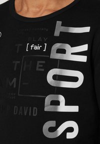 Camiseta de algodón negra con gran texto plateado en diferentes fuentes, que dice "DEPORTE", "[justo]" y varias frases. Diseño de cuello redondo.