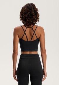 Čierny športový crop top s nastaviteľnými krížovými ramienkami, hladkou textúrou a logom, v kombinácii s čiernymi legínami s vysokým pásom.