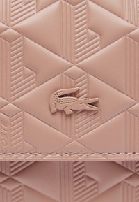 Cuir texturé rose avec un motif géométrique. Présente un logo de crocodile en relief et une couture contrastée le long du bord.