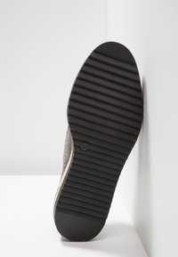 Semelle de chaussure avec rainures horizontales et taille 37 marquée, positionnée verticalement contre un mur d'angle blanc et le sol.
