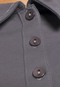 Szary materiałowy shirt o prążkowanej fakturze, z czterema ciemnobrązowymi guzikami i kontrastowym przeszyciem wzdłuż listwy guzikowej oraz kołnierzyka.