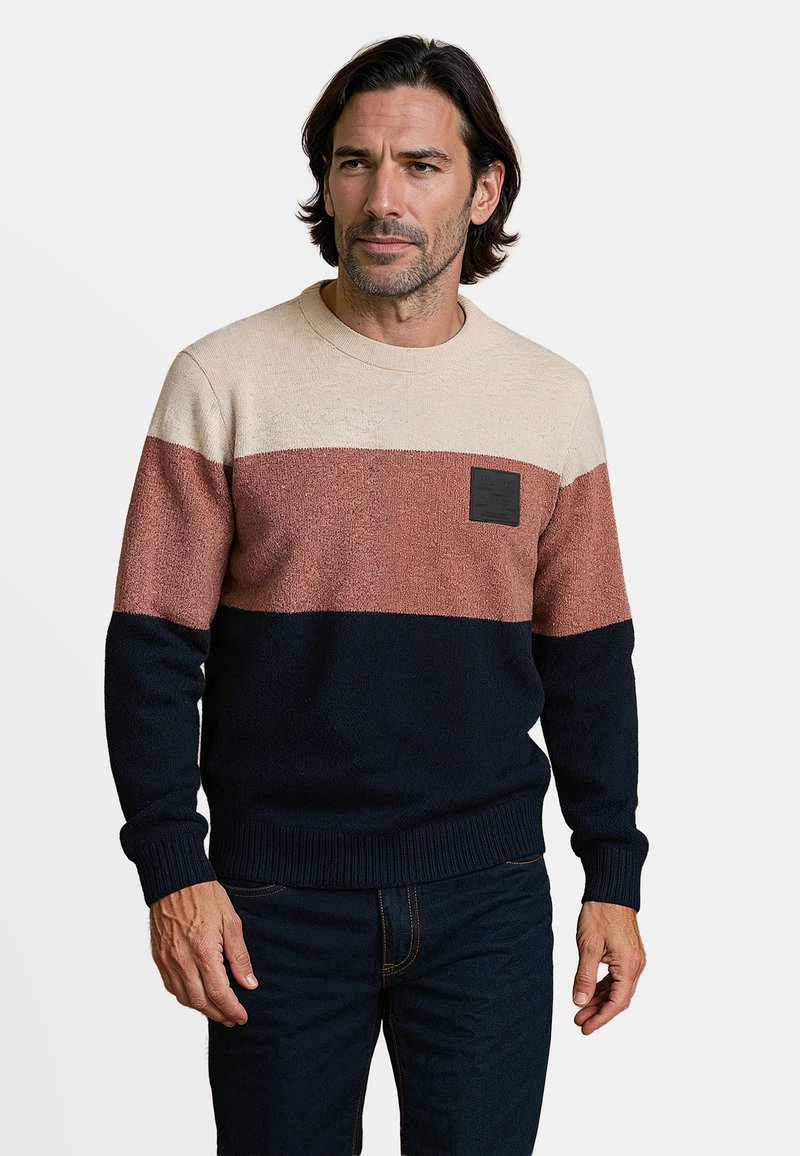 Gebreide trui met een beige, roest en marineblauwe gestreepte ontwerp, met een gestructureerde afwerking en een zwart merkembleem op de borst. Ribgebreide manchetten.