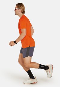 Orange kortærmet skjorte, grå løbeshorts med sidelapper, sorte sportssokker og hvide sneakers med orange detaljer.