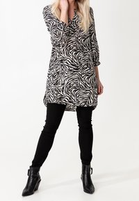 Black and white zebra print tunic with 3/4 sleeves, paired with black fitted pants and ankle boots, showcasing a loose, elongated silhouette.