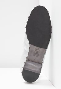 Semelle de chaussure en cuir blanc montrant une semelle en caoutchouc noir, empreinte de taille 4 et marquage "Echt Leder All Leather".