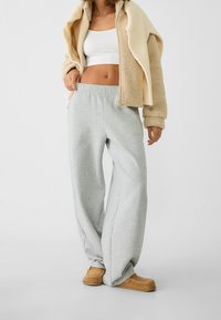 Jasnoszare, szerokie spodnie dresowe z elastycznym pasem, połączone z beżową kurtką z polaru i brązowymi butami w stylu mokasynów.