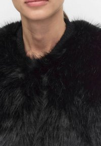 Svart fuskpälskrage med en mjuk, texturerad yta, som har en glänsande finish och en lurvig look, som omger nackområdet.