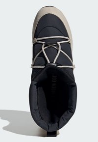 Vista superior de una bota de invierno aislada en negro y beige, con cordones elásticos y cuello acolchado.