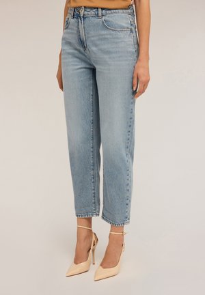 Jeans taille haute bleu clair avec une coupe décontractée, présentant des dégradés subtils et des ourlets retroussés, associés à des chaussures à talons hauts de couleur nude.