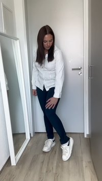White striped button-up shirt, navy blue skinny pants, and white sneakers with black accents; standing in front of a mirror and a light-colored wall.