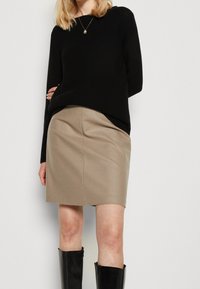 Zwarte gebreide trui gecombineerd met een beige kokerrok, met een soepele textuur en een getailleerde pasvorm. De look wordt compleet gemaakt met zwarte kniehoge laarzen.