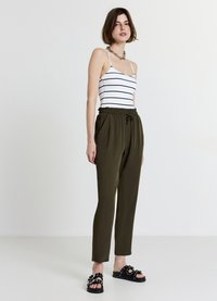 Top senza spalline a righe bianche e nere abbinato a pantaloni larghi verde oliva; sandali neri a ciabatta con borchie decorative e fiocchi.