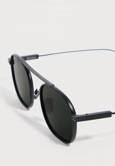 Black metal-framed sunglasses with dark round lenses and thin temples, shown against a plain light background.