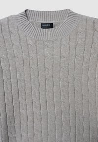 Pull en tricot gris clair avec un col rond côtelé et un motif en maille fantaisie. Texture douce, présentant des rangées verticales de motifs entrelacés.