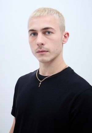 Čierne tričko vyrobené z bavlny, s okrúhlym výstrihom. Zlata reťaz s malým krížovým príveskom sa nachádza okolo krku.