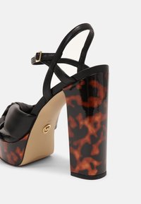 Sandales à plateforme en cuir noir avec un talon à motif écaille de tortue. Présente un design à lanières croisées et des détails en métal doré.