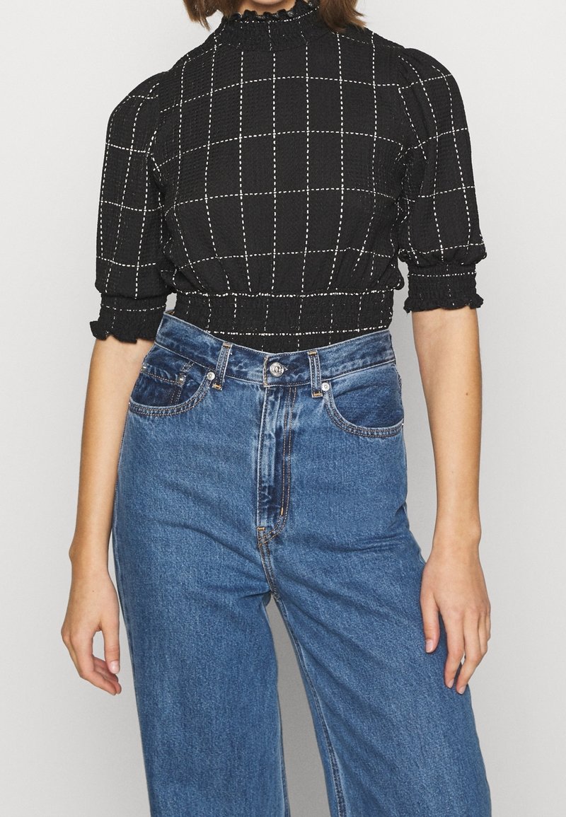 Zwart geruite cropped top met pofmouwen en een ruches halslijn, gecombineerd met hoge blauwe denim jeans.