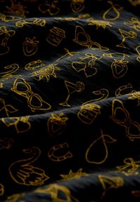 Sort stof med gule broderede mønstre, herunder solbriller, sol, cocktails, frugt og forskellige finurlige motiver.