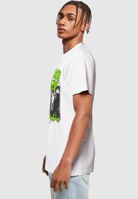 Hvid bomulds t-shirt med grøn grafisk print og sort grafik. Korte ærmer, afslappet pasform og rund hals.
