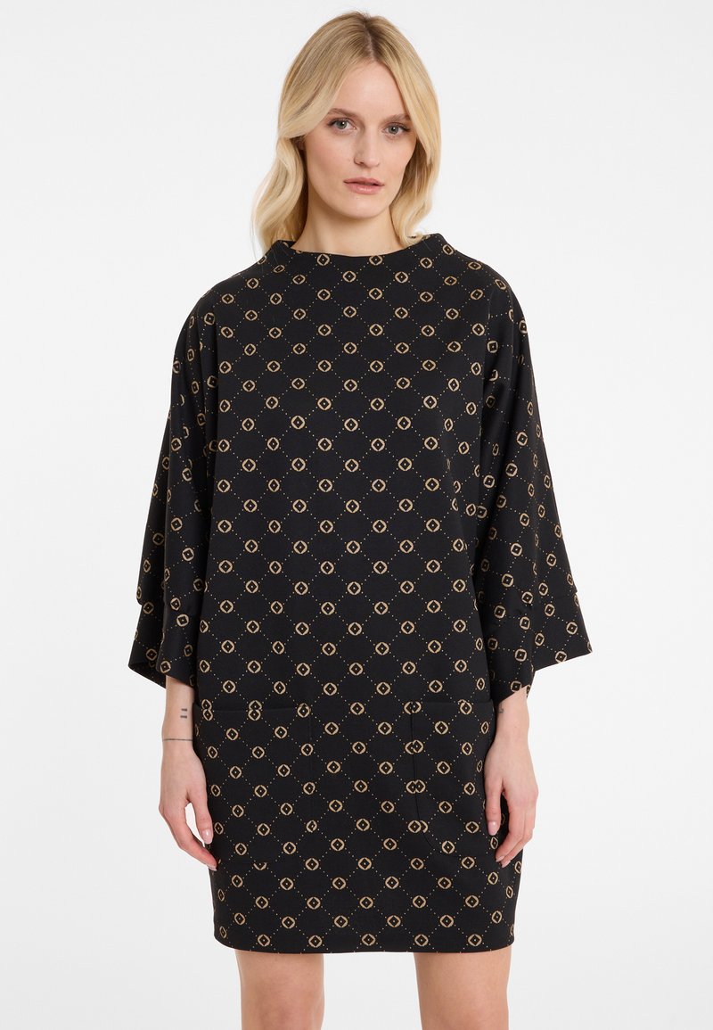 Zwarte jurk met een geometrisch gouden patroon, korte batwing mouwen en een relaxte pasvorm. Gemaakt van zachte stof met een gladde textuur.