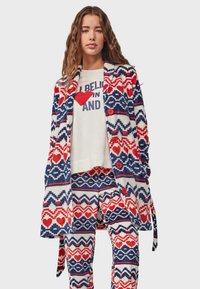 Patterned knit cardigan in red, blue, and white with heart motifs; paired with a graphic tee and matching pants featuring similar designs.