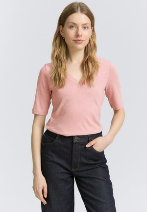 T-shirt a maniche corte di un rosa chiaro con scollo a V abbinato a jeans denim blu scuro, caratterizzati da una vestibilità rilassata e una sottile texture del tessuto.